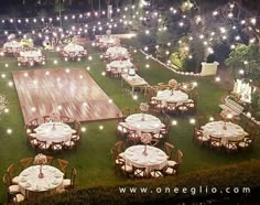 tables and chairs are set up on the lawn for an outdoor event with string lights