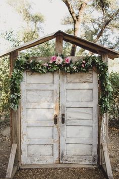 an old wooden door with flowers on the top and bottom is surrounded by greenery