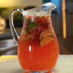 a pitcher filled with liquid and garnished with limes, orange slices and cilantro