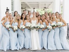 a group of women standing next to each other in front of a white building holding bouquets