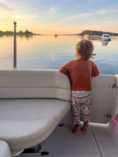 a little boy standing on the back of a boat looking out over water at boats