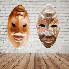 two masks sitting on top of a wooden floor in front of a brick wall,