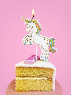 a piece of cake with a unicorn candle on top is sitting in front of a pink background