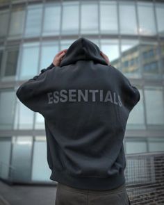 a man standing in front of a building with the words essential written on his hoodie