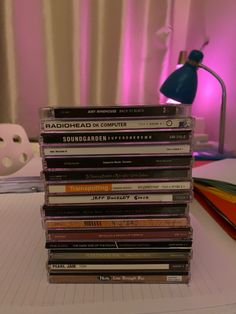 a stack of cds sitting on top of a table next to a lamp and book