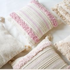 four pillows with tassels are arranged on a white surface, one is pink and the other is beige