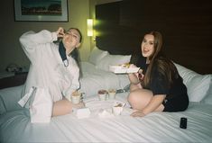 two women sitting on a bed eating food