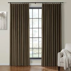 a living room with a white chair and large window covered in dark brown drapes