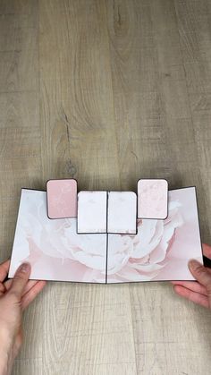 two hands are holding an open box with four different designs on it and one is pink