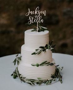 a white wedding cake with greenery on top and the word'the godday'written in cursive letters