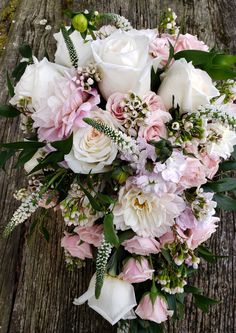 a bouquet of white and pink flowers sitting on top of a wooden table with greenery