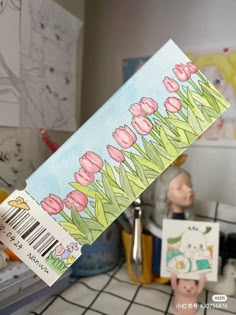 a person holding up a piece of paper with flowers painted on it in the background