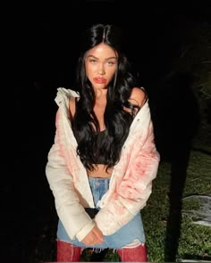 a woman standing in the dark with her hands on her hips and wearing ripped jeans