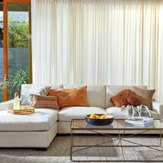 a living room with white couches, orange pillows and a coffee table in front of a window