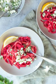 two white bowls filled with red pasta and garnished with feta cheese on top