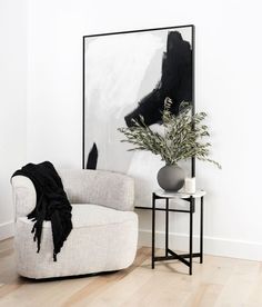 a black and white abstract painting hangs in the corner of a room next to a chair