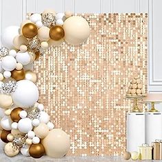 a table topped with lots of white and gold balloons next to a wall covered in sequins