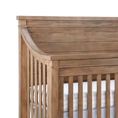 a wooden crib with white sheets on the bottom and side rails, against a white background