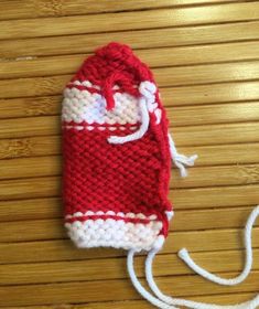 a red and white knitted bag sitting on top of a wooden floor next to a string