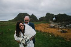 a man and woman standing next to each other in front of some rocks on the grass