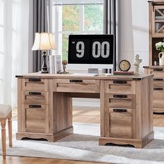 a wooden desk with a clock on it in front of a window and a chair