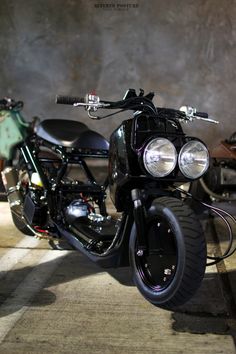 two motorcycles parked next to each other in a room with concrete walls and flooring