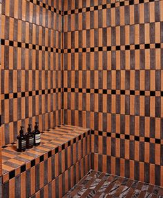 two bottles are sitting on a shelf in a tiled room with black and brown tiles