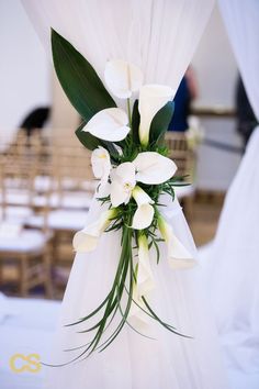 white flowers and greenery are arranged on the back of a wedding ceremony chair cover