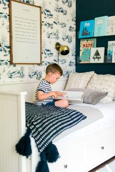 a young boy sitting on top of a white bed in a blue and white bedroom