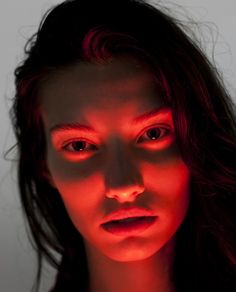 a woman's face lit up with red light from her eyes and hands, in front of a white background