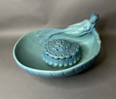 a blue bowl with a shell in the shape of a woman sitting on top of it