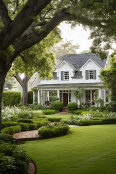 a large white house surrounded by lush green grass and trees with lots of bushes around it