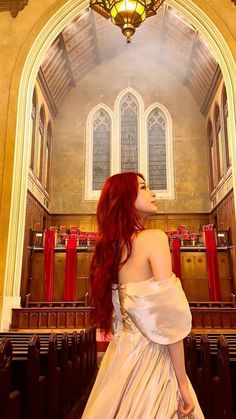 a woman with long red hair standing in front of a church pew and looking up at the ceiling