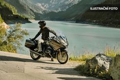 a man riding on the back of a motorcycle down a road next to a lake