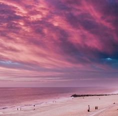 people walking on the beach at sunset with pink clouds in the sky over the water