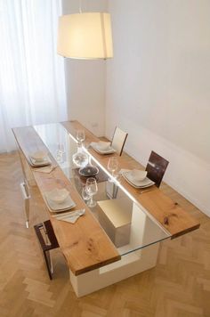 a glass table with wooden chairs and plates on it in the middle of a room