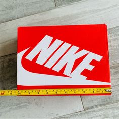 a red nike box sitting on top of a wooden floor next to a measuring tape