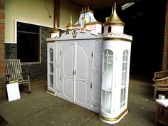 a white and gold doll house sitting on top of a floor next to a bench