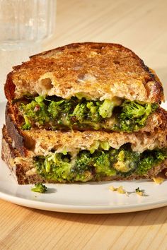 a grilled cheese and broccoli sandwich on a plate with a glass of water