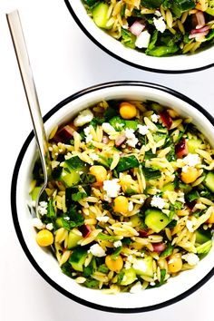 two bowls filled with pasta and vegetables on top of a white countertop next to each other