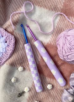 two crochet hooks are laying on a blanket next to balls of yarn and knitting needles