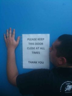 a man leaning against a blue wall with a sign on it that says, please keep this door close at all times thank you