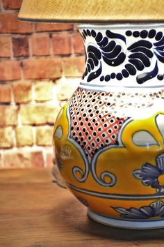 a yellow and blue vase sitting on top of a wooden table next to a lamp