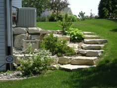 a garden with rocks and plants on the side of it, in front of a house