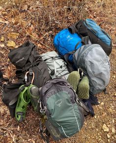 several backpacks and shoes laying on the ground in front of some dry grass with leaves