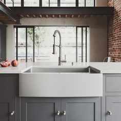 a kitchen with gray cabinets and a white sink in front of an open brick wall