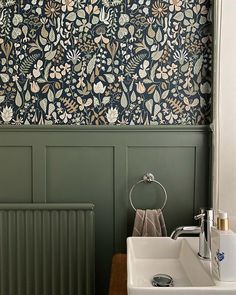 a bathroom with green walls and floral wallpaper in the corner, along with a white sink