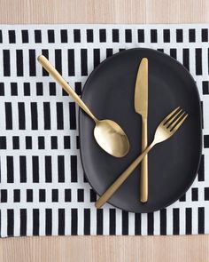 a black plate with gold forks and spoons sitting on top of a white and black place mat