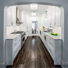 a kitchen with white cabinets and wood floors is seen through an arch in the wall