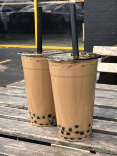 two iced coffees sitting on top of a wooden table next to each other in front of a parking lot